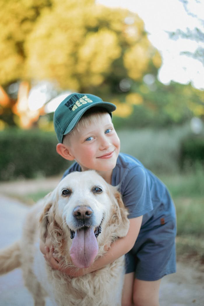 A joyful child in a blue outfit hugs a happy golden retriever outside on a sunny day.